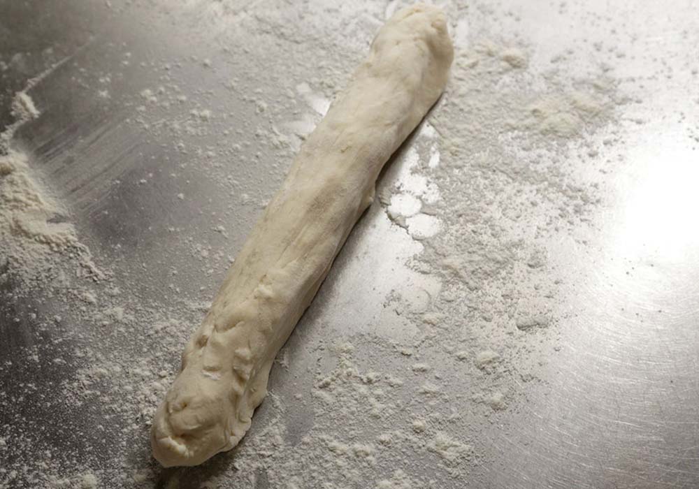 多めに打ち粉をした台に生地を取り出す。手で引っ張って棒状に伸ばし、三等分に分割する。 POINT：軟らかいので引っ張って伸ばせる。