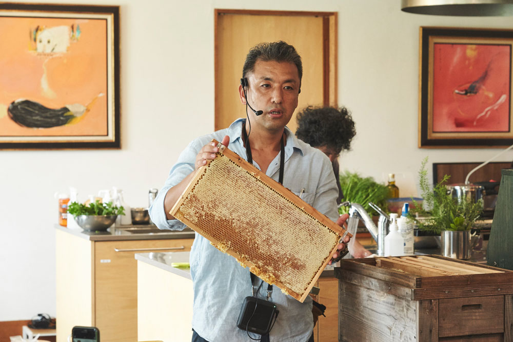 持参した巣箱で、ハチの巣の形成過程を解説。「巣作りには蜜蝋が不可欠ですが、蜜蝋１ｇ生み出すのに、その10倍のハチミツを必要とします。だから、巣脾（すひ。蜜をためる枠のこと）をできるかぎり使い続けます」。