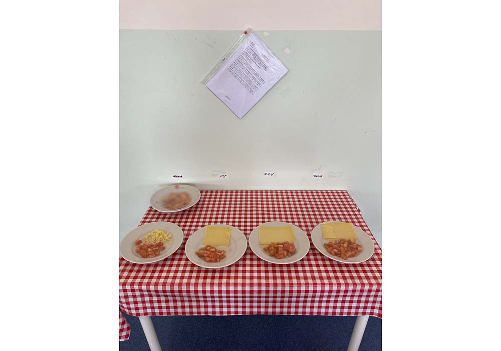 配膳スタッフ間でメニューの量と盛り付けを共有するため、見本が給食室の一角に毎日展示される。左から幼稚園、小学１～２年生、３～５年生、中学初年度生の盛り付け例。