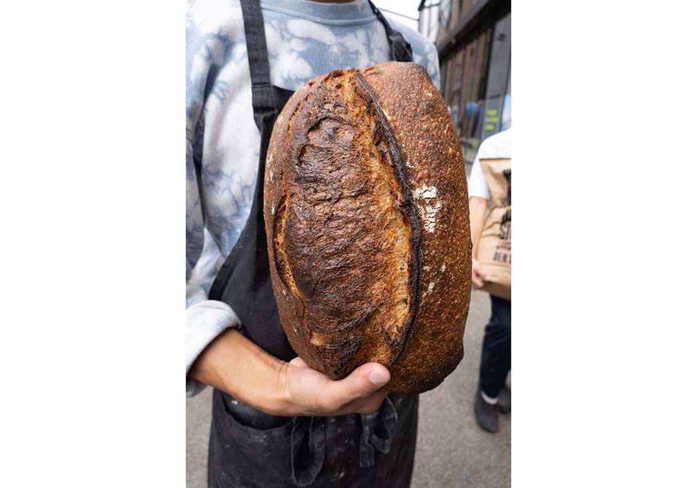 (写真)スウェーデン・オーランド島原産の在来種、オーランド小麦を20～30％配した「20% オーランド（Øland）」。イレブロで一番全粒粉の割合が少ないパンだ。「味がしっかりしたオーランド小麦を長時間発酵させて焼いているので、クラストは食べると繊細にはじけながら香ばしさと甘味を感じ、クラムからは乳酸菌発酵による長い余韻と小麦が持つ旨味が感じられます。1.3kgの重さがありますが、スライスすると食べやすく、サワードウが持つ奥行きを感じやすい。どんな食べ方にも料理にも合うので、初めて来た方にはまずはこのパンをお勧めしています」