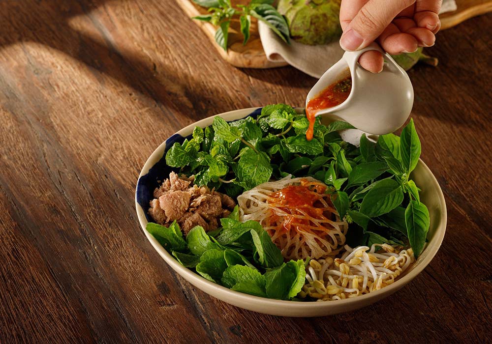 （写真）「タピオカ・ヌードル　スパイシーソース」（180,000ドン）。南中部クアンナム省クエソン県のタピオカから作るタピオカ麺は、失われつつある伝統食材。同省の古都ホイアン・トラケ村で有機栽培されたフレッシュハーブとシャキシャキした食感の長もやしを使用する。スパイシーソースはゴマ、コリアンダー、青唐辛子など10種類の地元産香辛料をブレンドした香り高いオリジナルレシピ。