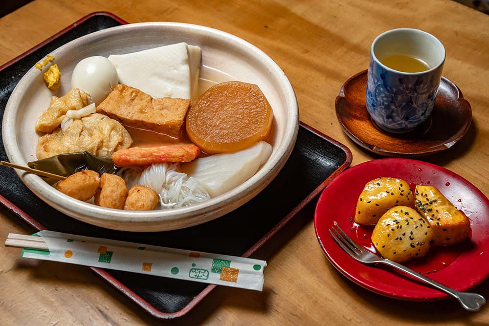 おでんのだしは、煮干しと昆布。ほんのり甘く、澄んだ味わいで、「うちは酒のアテとしてじゃなく、夕食やおやつに食べるおでんだから」と醤油は仕上げに１、２滴加える程度。「あとは練り物の味がだしに染みてくる」。８時間煮詰めた蜜を絡める大学芋は、ビジネス用のお土産としても人気。