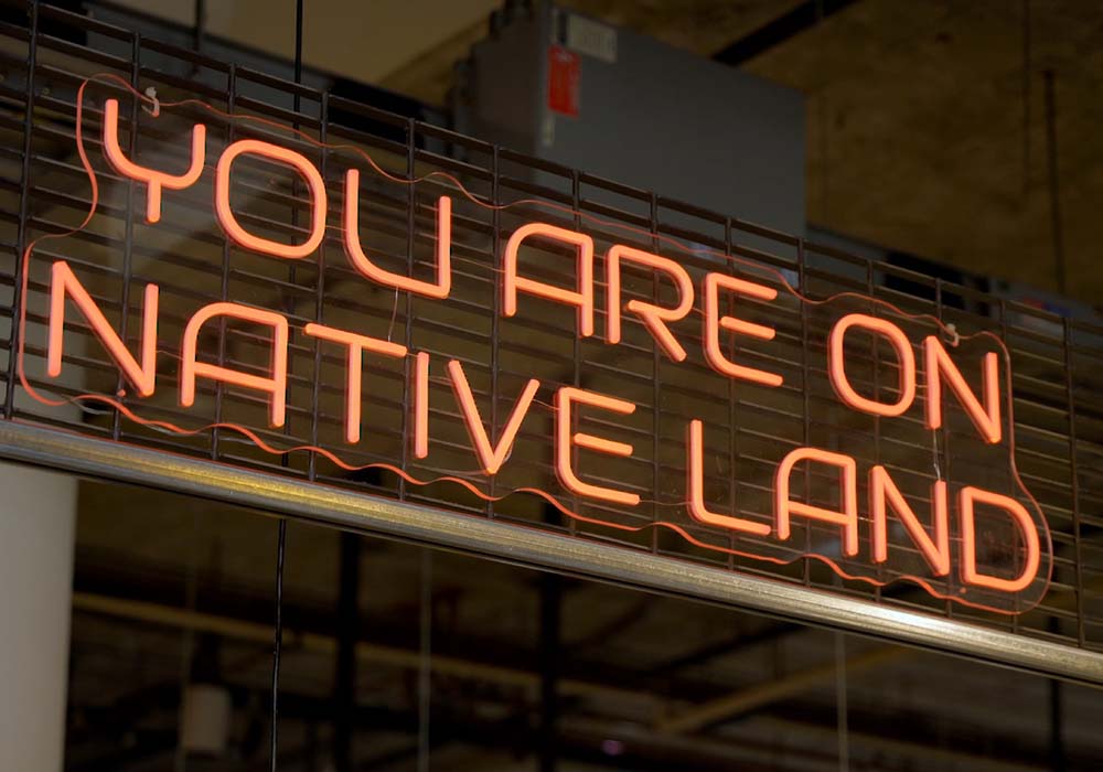 (写真)「あなたは先住民の土地に立っている」――インディジネス・フードラボ・マーケットの店頭に掲げられたサイン。訪れる人々に、この店のあるエリアがミネアポリスのミッドタウンになる前の風景と、欧州人が入植する前の歴史に思いを馳せてもらうのが目的だ。photograph by Sergio Rapu