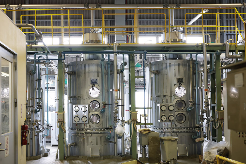 クラリファイヤーで沈殿・濾過後、タンク（写真）に入れて徐々に減圧しながら加熱し、糖度72～73°brixになるまで煮詰める。その後、ふるい機で不純物を取り除き、ロートサム（遠心薄膜式濃縮器）を通してさらに炊き上げ、どろどろの状態に。これをベルトコンベアにのせてこねるようにし、ブロックや粉末状の黒糖に仕上げていく。