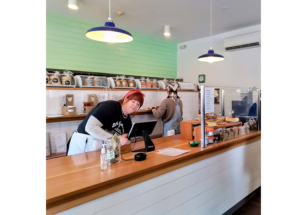 （写真）カウンター奥には持ち帰り用イングリッシュマフィンがずらりと並ぶ。プレーンな「クラシック」、「フレンチトースト」、モラセスとコーンミールを使ったニューイングランド地方特有のパンを再現した「アナダマ」、ベーグルでお馴染みのガーリック、オニオン、ゴマ、ケシの実をまぶした「エブリシング」、そしてヴィーガンの「マルチグレイン」と「オーツ麦＆セサミ」の６種類（各４個入り９ドル）。レジ横には、クッキーや焼き菓子等も並んでいる。