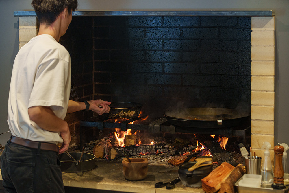 右側でパエリア、左側でキノコのソテーを調理中。ちなみに料理しているのは調理師学校時代の同期生でイタリア修業を経て一時帰国中の小山拓夢さん。10月末、ロンドンへ旅立って行った。